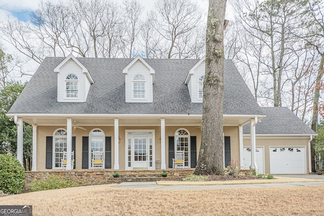 cape cod-style house with ceiling fan, roof with shingles, covered porch, stucco siding, and an attached garage