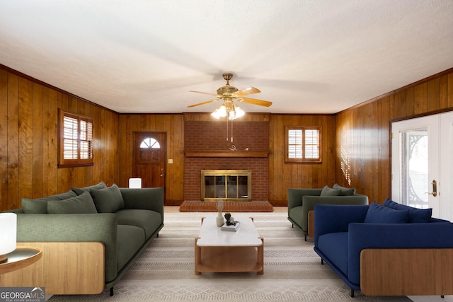 living room with wooden walls, ceiling fan, a brick fireplace, and a healthy amount of sunlight