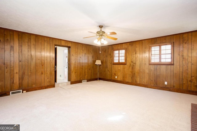 empty room featuring wooden walls, baseboards, a ceiling fan, and visible vents