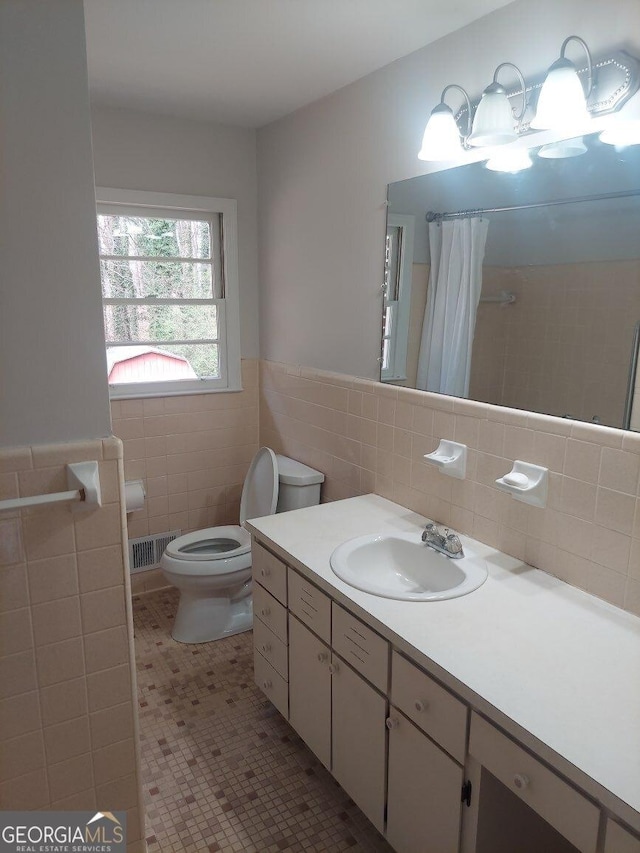 full bathroom featuring vanity, toilet, visible vents, wainscoting, and tile walls