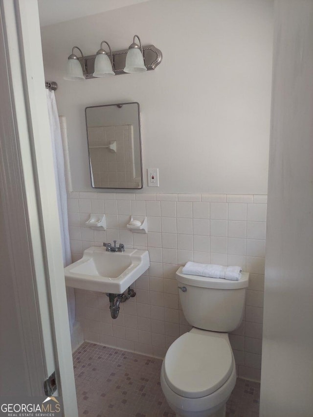 bathroom featuring wainscoting, tile walls, a sink, and toilet