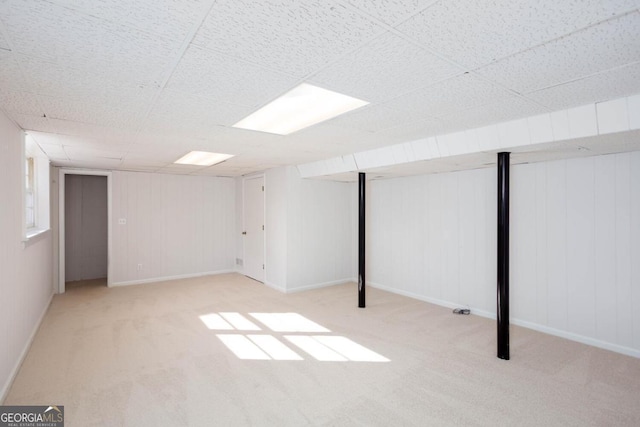 finished below grade area featuring a paneled ceiling, baseboards, and carpet