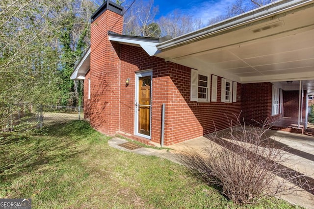 view of property exterior featuring a yard, a chimney, fence, brick siding, and an attached carport