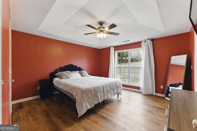 bedroom with a raised ceiling, ceiling fan, baseboards, and wood finished floors