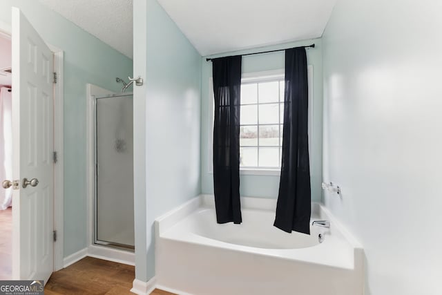 full bathroom featuring a stall shower, baseboards, a bath, and wood finished floors