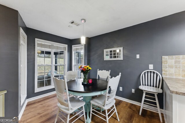 dining space featuring an accent wall, visible vents, baseboards, and wood finished floors