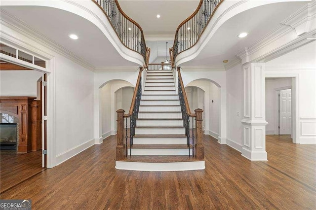 stairway with arched walkways, wood finished floors, and crown molding