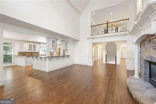 living area with arched walkways, a stone fireplace, dark wood-style flooring, ornamental molding, and decorative columns