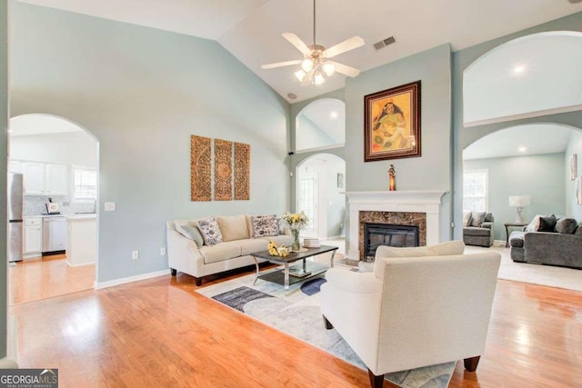 living room with a wealth of natural light, visible vents, high vaulted ceiling, light wood-style flooring, and a high end fireplace