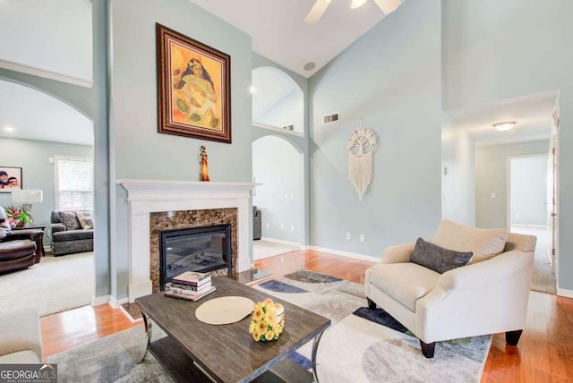 living area featuring arched walkways, a fireplace, a towering ceiling, and wood finished floors