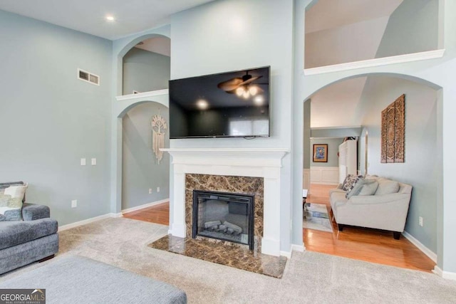 living room with baseboards, visible vents, a high ceiling, a high end fireplace, and carpet flooring