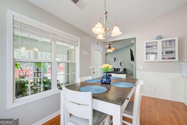 dining space featuring ceiling fan with notable chandelier, wood finished floors, visible vents, and baseboards