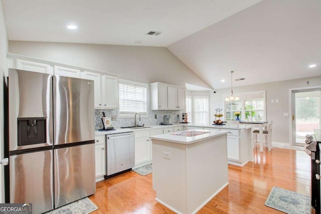 kitchen with a peninsula, a sink, stainless steel appliances, light countertops, and a center island