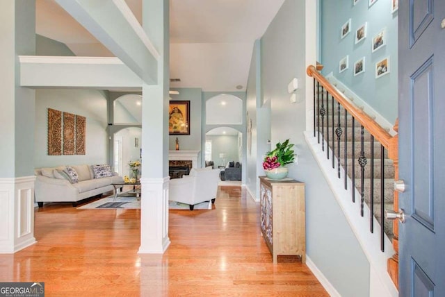 entrance foyer with stairs, light wood-type flooring, a fireplace, a towering ceiling, and arched walkways