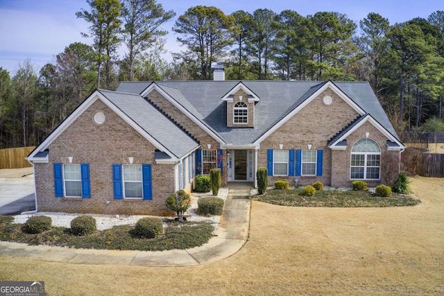 view of front facade with brick siding, a chimney, and fence