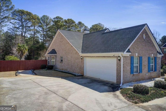 view of property exterior featuring fence, a chimney, concrete driveway, a garage, and brick siding