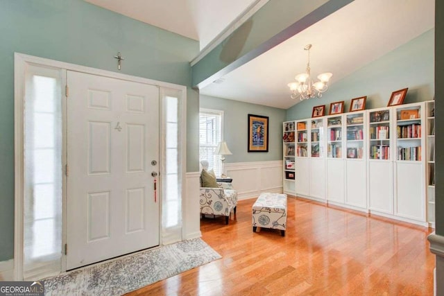 entryway featuring lofted ceiling, wainscoting, an inviting chandelier, wood finished floors, and a decorative wall