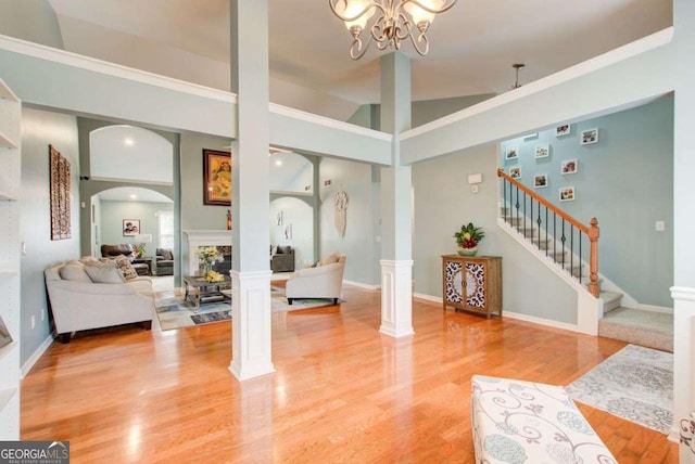 living room featuring light wood-type flooring, stairway, arched walkways, a stone fireplace, and decorative columns