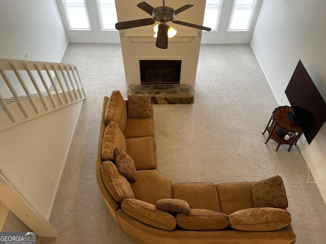 carpeted living area with a fireplace with raised hearth, ceiling fan, baseboards, and a healthy amount of sunlight