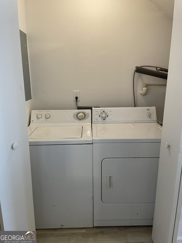 clothes washing area featuring laundry area, wood finished floors, washing machine and dryer, and electric panel