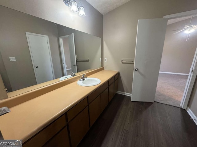 bathroom with lofted ceiling, a textured ceiling, vanity, wood finished floors, and baseboards