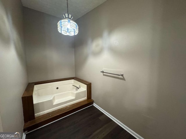 bathroom featuring a garden tub, a textured ceiling, wood finished floors, and baseboards