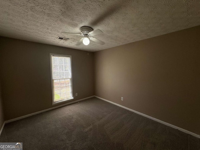 empty room with dark colored carpet, visible vents, a ceiling fan, a textured ceiling, and baseboards