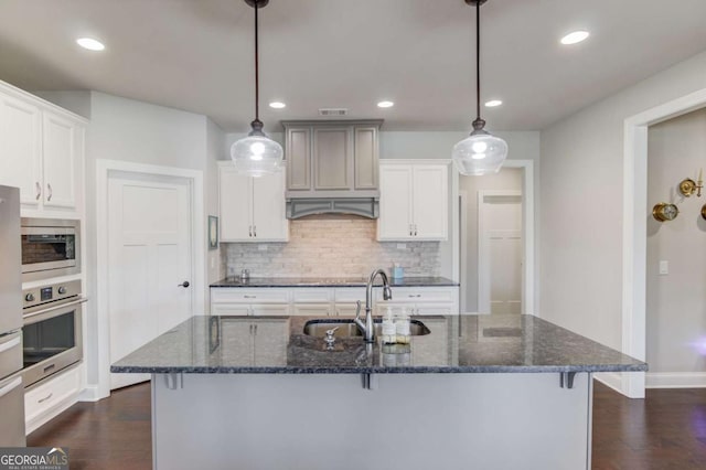 kitchen with a sink, appliances with stainless steel finishes, decorative backsplash, dark wood finished floors, and pendant lighting