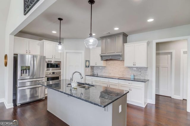 kitchen with dark wood-style floors, tasteful backsplash, appliances with stainless steel finishes, a sink, and an island with sink