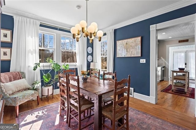 dining room with a healthy amount of sunlight, crown molding, an inviting chandelier, and wood finished floors