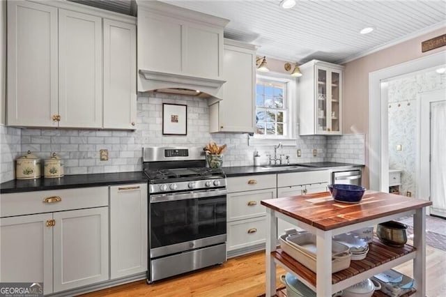 kitchen with dark countertops, appliances with stainless steel finishes, glass insert cabinets, custom exhaust hood, and a sink