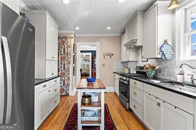 kitchen with light wood-style flooring, stainless steel appliances, a sink, decorative backsplash, and crown molding