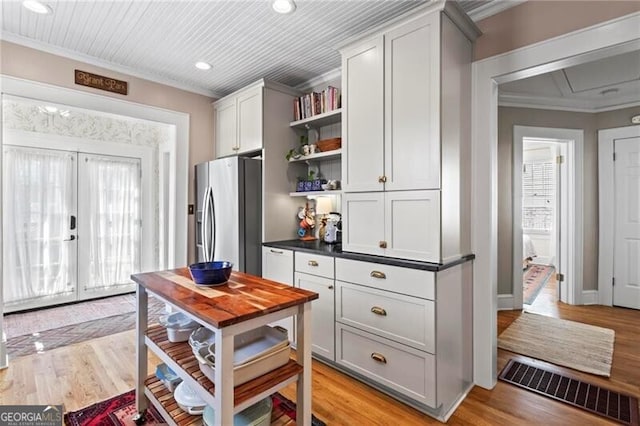 kitchen with crown molding, open shelves, dark countertops, visible vents, and stainless steel fridge