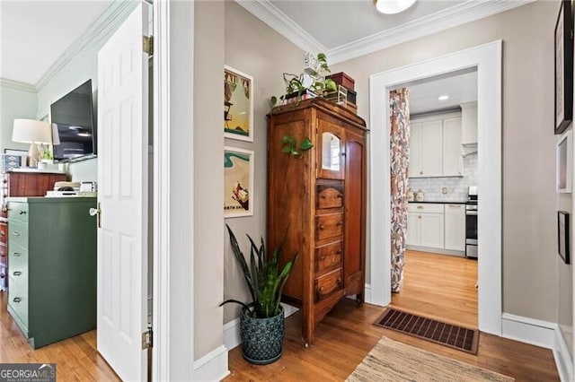 hall featuring baseboards, light wood-style floors, visible vents, and crown molding