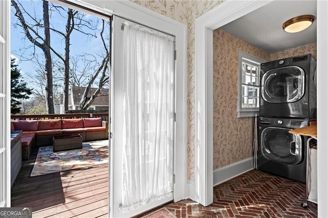 laundry room featuring brick floor, stacked washer / drying machine, laundry area, and wallpapered walls