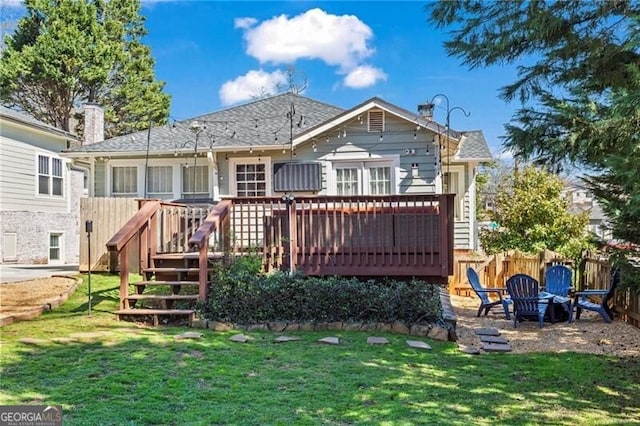 rear view of property with an outdoor fire pit, a lawn, fence, and a wooden deck