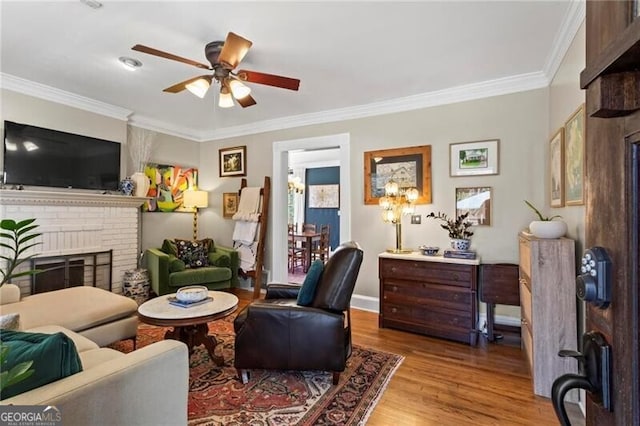 living room with baseboards, a ceiling fan, wood finished floors, crown molding, and a brick fireplace