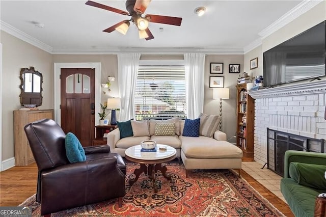 living room featuring ornamental molding, a brick fireplace, ceiling fan, wood finished floors, and baseboards