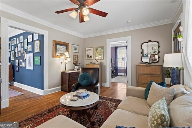 living room with a ceiling fan, crown molding, baseboards, and wood finished floors