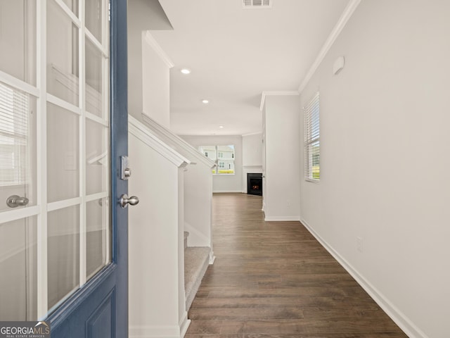 entryway with dark wood-style floors, visible vents, a warm lit fireplace, stairs, and crown molding