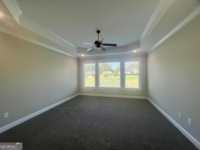 empty room featuring a raised ceiling, dark carpet, ornamental molding, ceiling fan, and baseboards