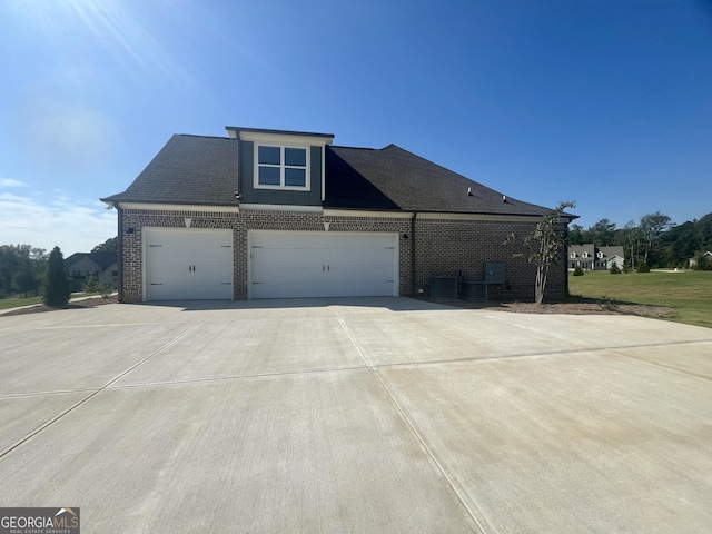 view of front of home featuring a garage, concrete driveway, brick siding, and roof with shingles