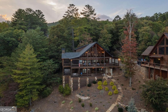 back of property with driveway, stairs, a chimney, and a view of trees