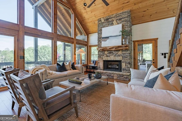 living room with wooden ceiling, wood finished floors, a stone fireplace, wood walls, and high vaulted ceiling