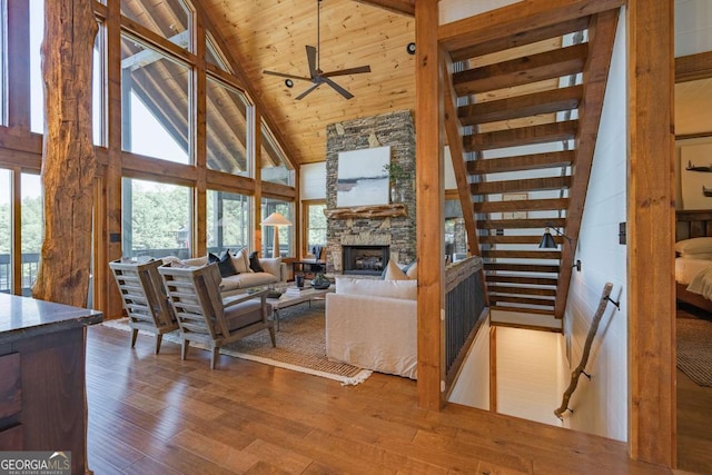 living room with high vaulted ceiling, a stone fireplace, wooden ceiling, wood finished floors, and stairs