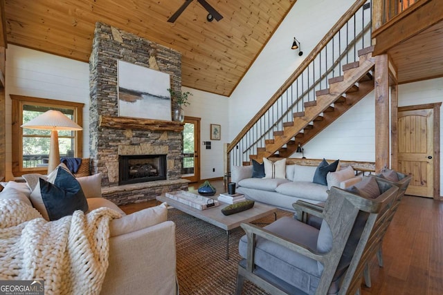 living area featuring wood-type flooring, stairway, a stone fireplace, high vaulted ceiling, and wooden ceiling