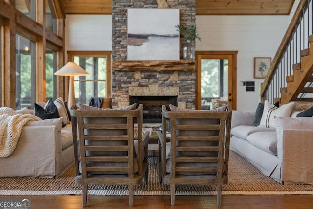 living room featuring wood-type flooring, wood walls, a stone fireplace, and stairs