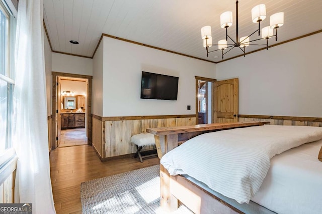 bedroom with a notable chandelier, wood walls, wood finished floors, ornamental molding, and wainscoting