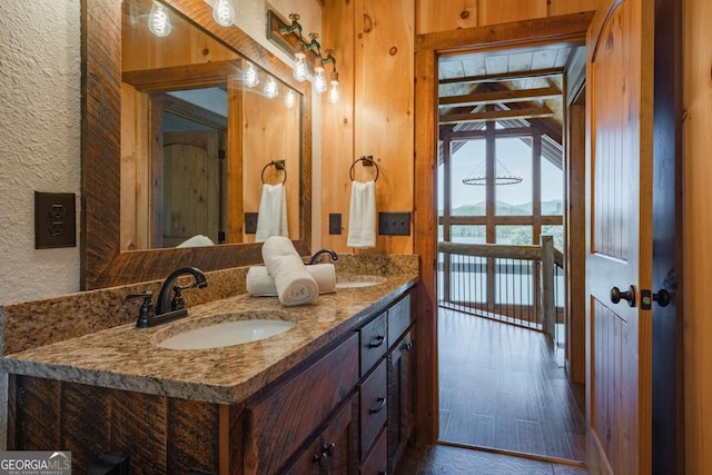 bathroom featuring a textured wall, double vanity, beamed ceiling, and a sink