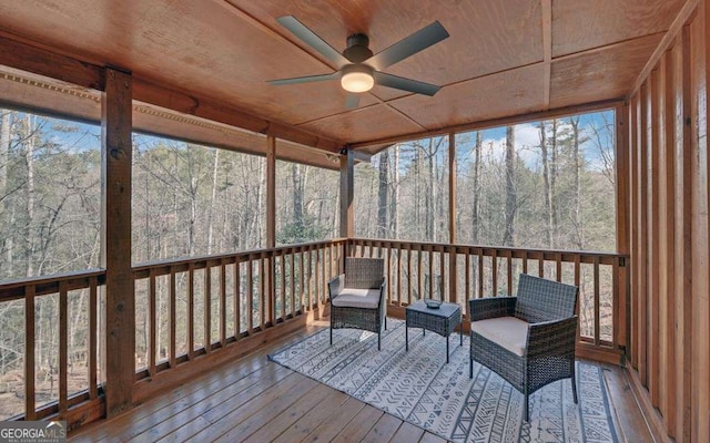 unfurnished sunroom featuring plenty of natural light, a view of trees, wooden ceiling, and a ceiling fan